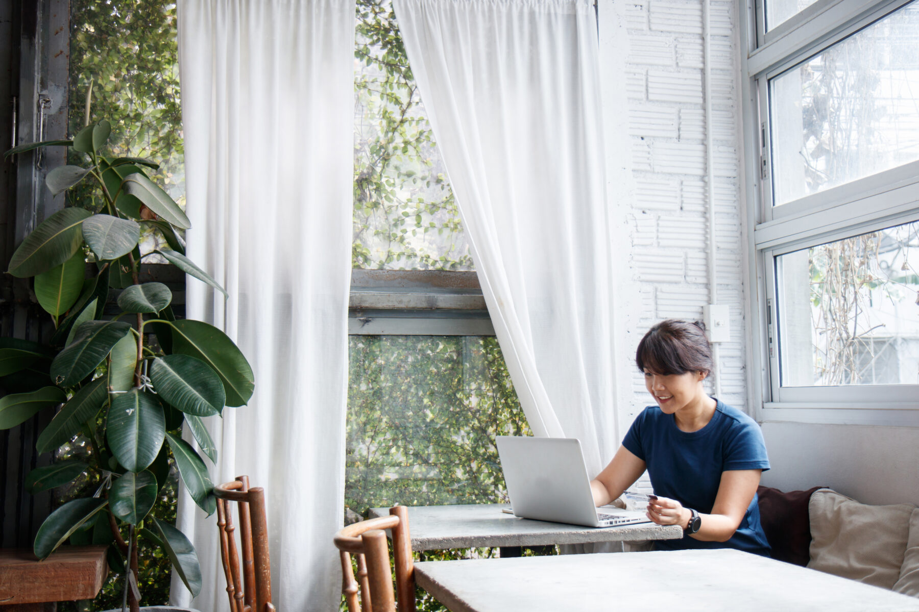 Asian young woman holding credit card and using laptop computer while sitting in cafe. Online shopping concept. Copy space.